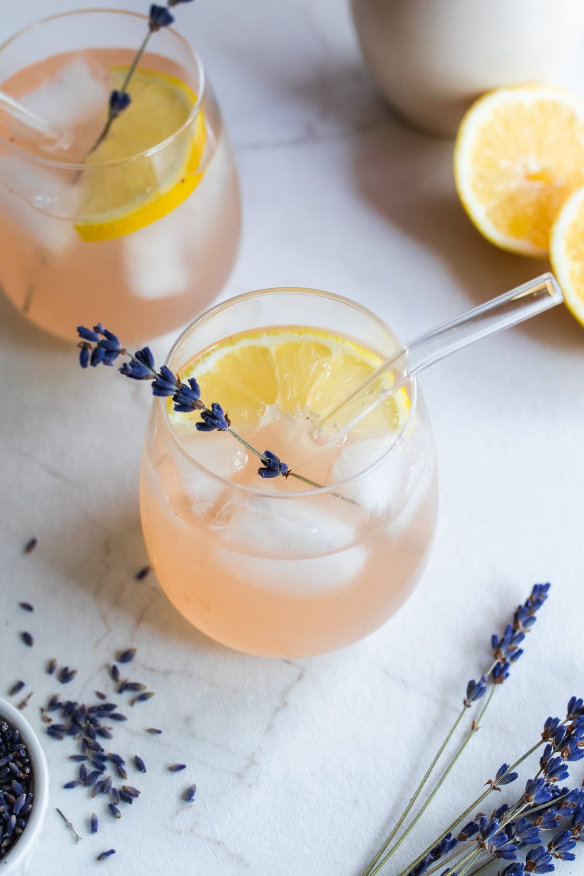 A glass of lemonade with a sprig of lavender and diced lemons in the glass.
