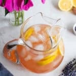 a glass pitcher with lemonade and ice cubes sitting on a countertop.