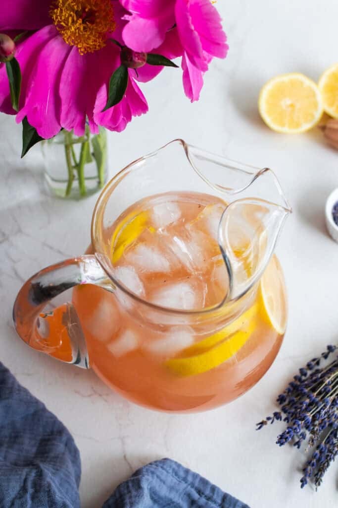 A glass pitcher with lemonade and ice cubes sitting on a countertop.