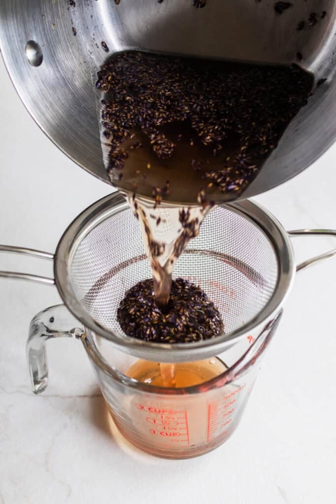 Straining lavender syrup through a mesh sieve.