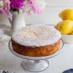 a cake dusted in powder sugar placed on a glass cake stand.