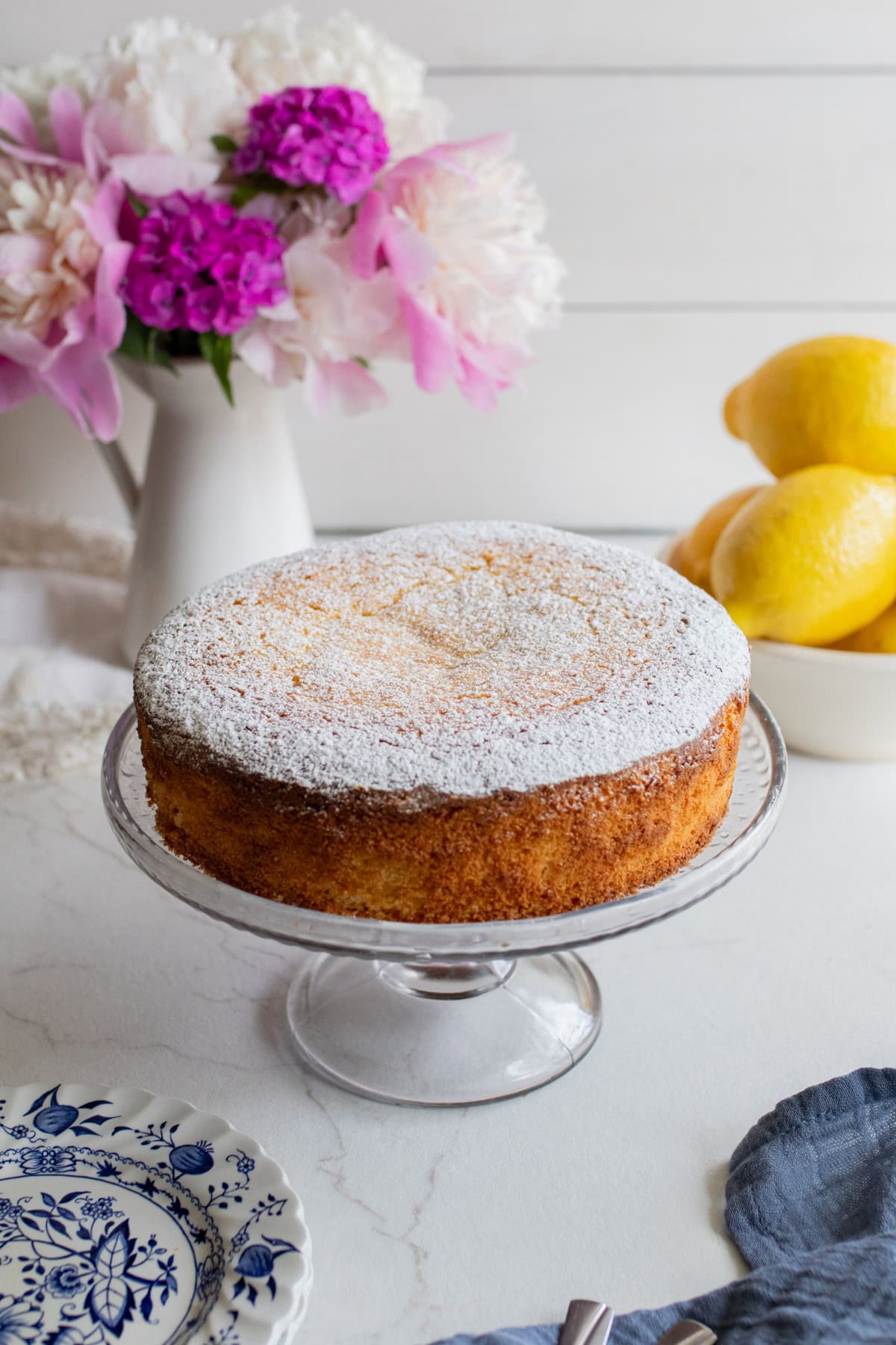 A lemon olive oil cake dusted in powder sugar placed on a glass cake stand.