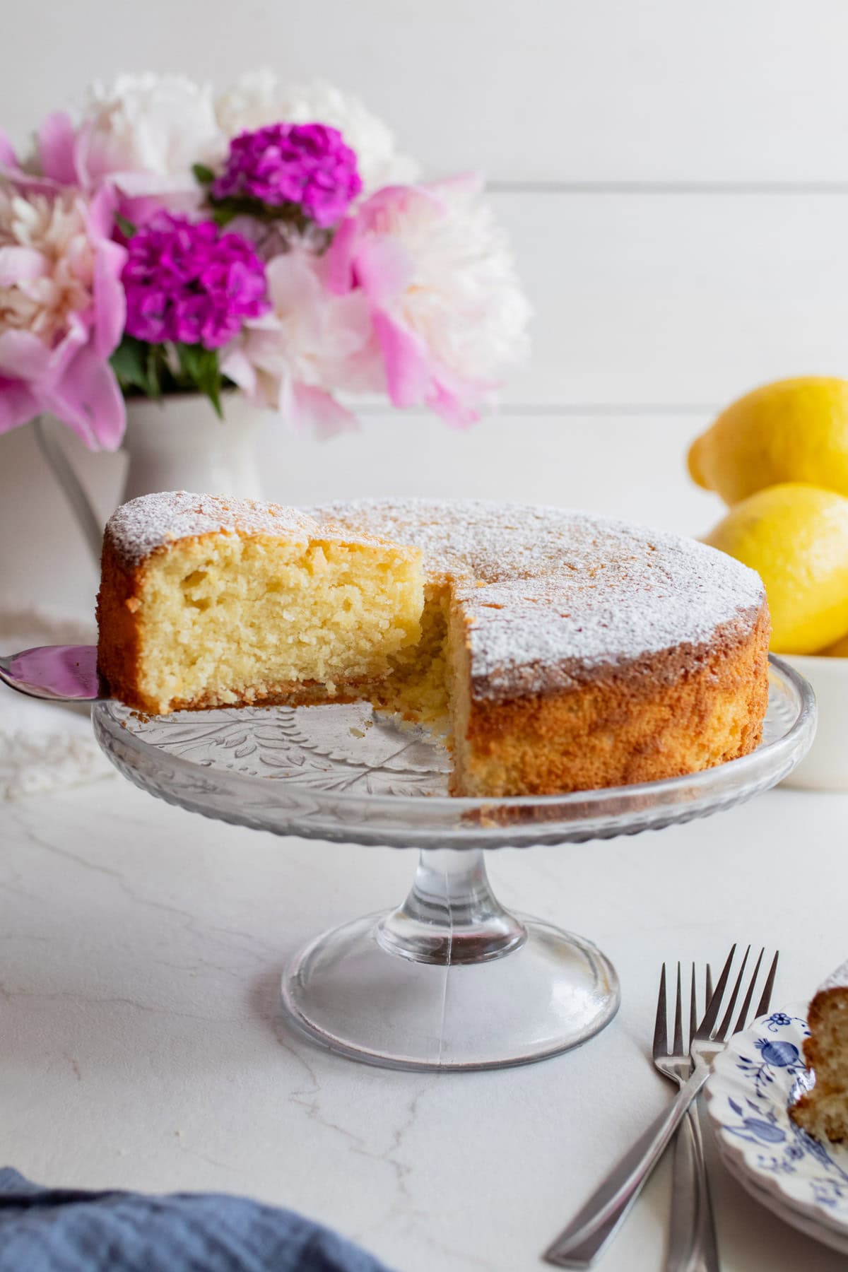A sliced lemon olive oil cake sitting on a glass cake plate.