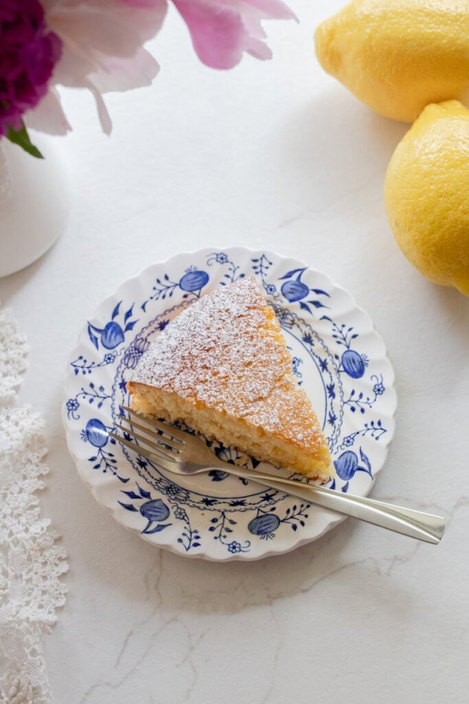 A slice of lemon olive oil cake dusted with powdered sugar on a plate.