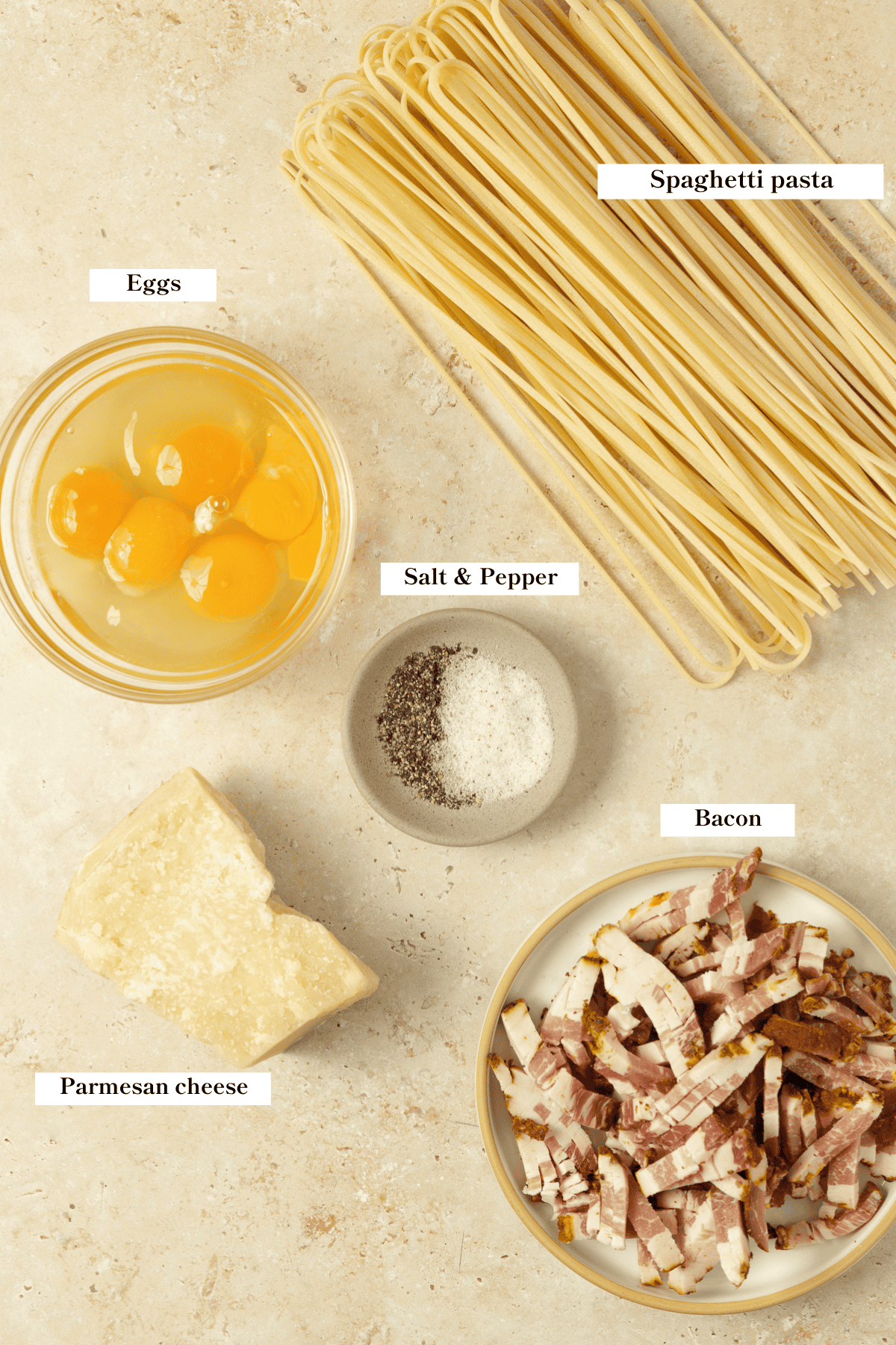 Noodles, bacon, eggs, parmesan, salt, and pepper on a kitchen counter.