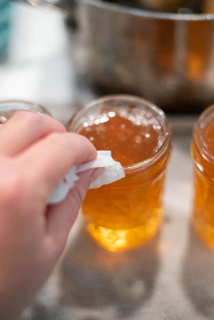 Wiping the rim of a peach jelly jar before sealing.