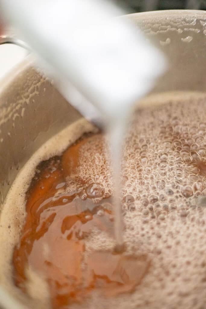 Pouring in liquid pectin into a large pot of peach and lemon juice.