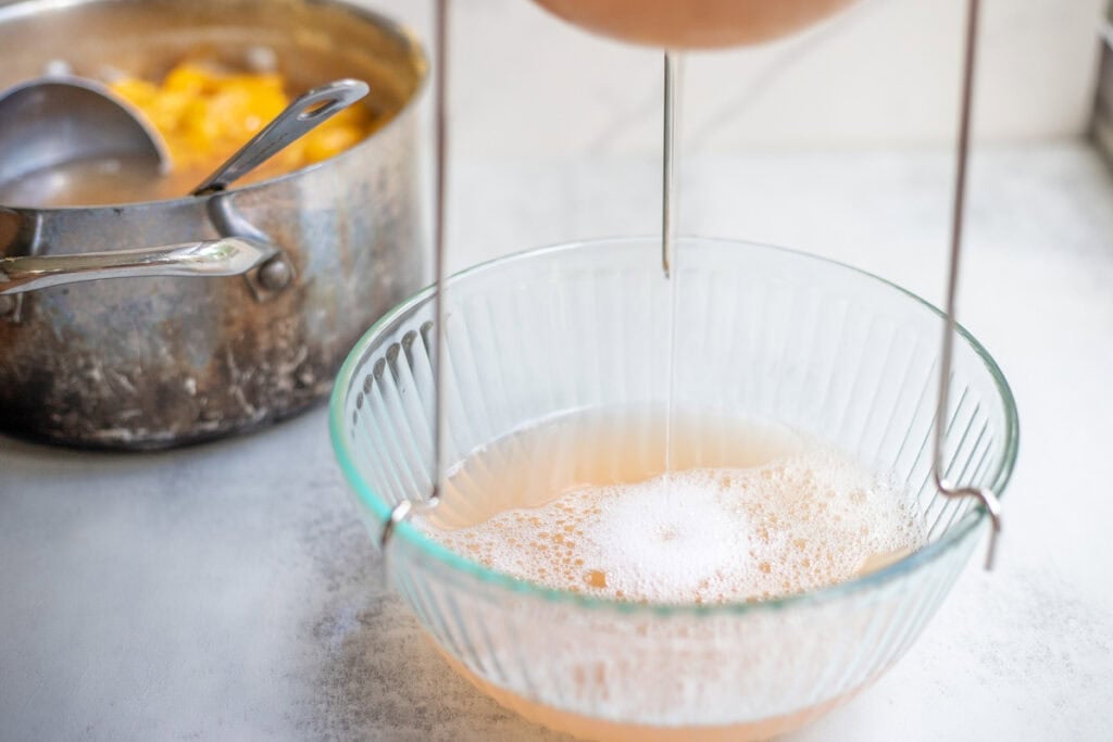 Peach juice straining into a glass bowl.