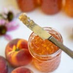 a jelly coated knife resting on a jar of peach jelly.