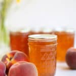 pint jars of peach jelly with a few peaches in front of the jar.