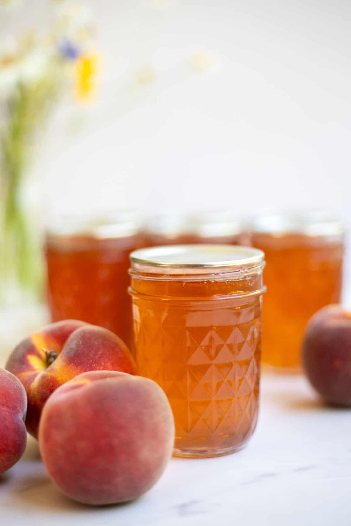 Pint jars of peach jelly with a few peaches in front of the jar.