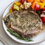a cooked pork chop in herbs on a white plate with vegetables.