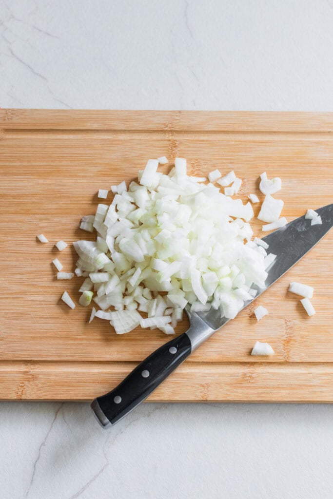 Diced onions on a cutting board with a knife to the right.