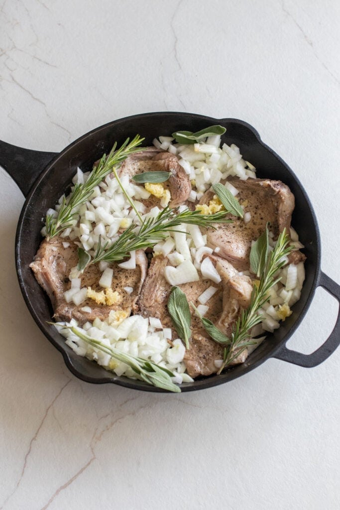 Pork chops in a skillet with fresh herbs, onions, and garlic.