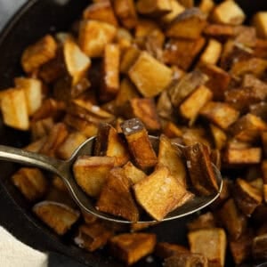 a spoon is taking out cooked potatoes from a cast iron skillet.