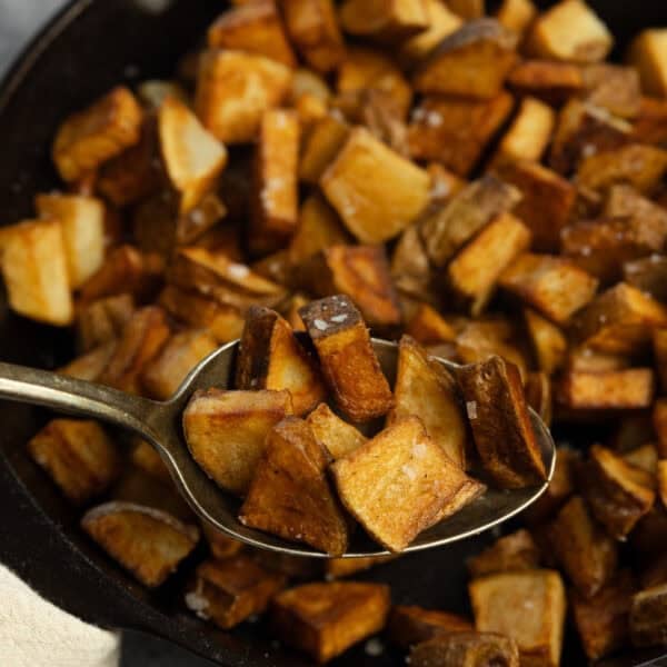 a spoon is taking out cooked potatoes from a cast iron skillet.