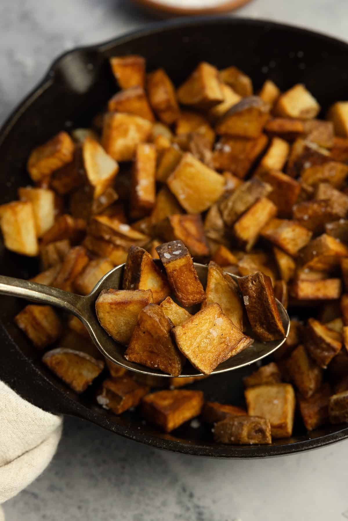 A spoonful of cooked potatoes over a cast iron skillet.