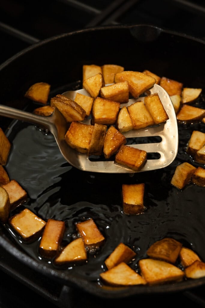 Cooked potatoes being flipped in a cast iron skillet.
