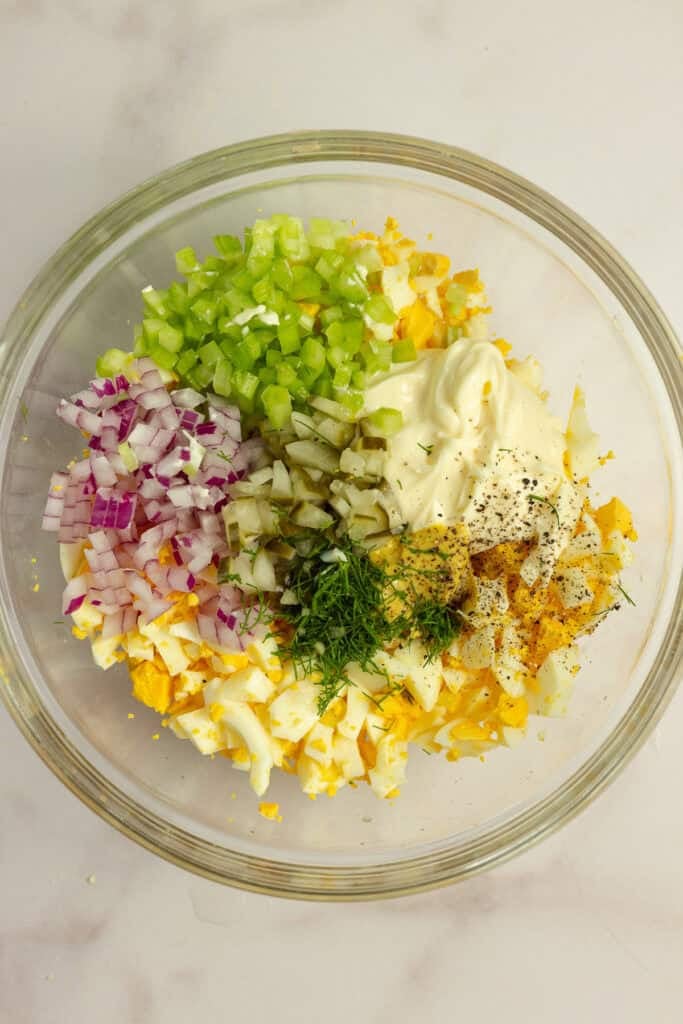 Chopped eggs, pickles, onions, and celery in a glass bowl.