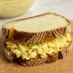 an egg salad sandwich sitting on a cutting board.