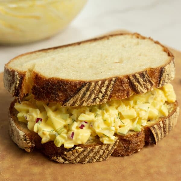an egg salad sandwich sitting on a cutting board.