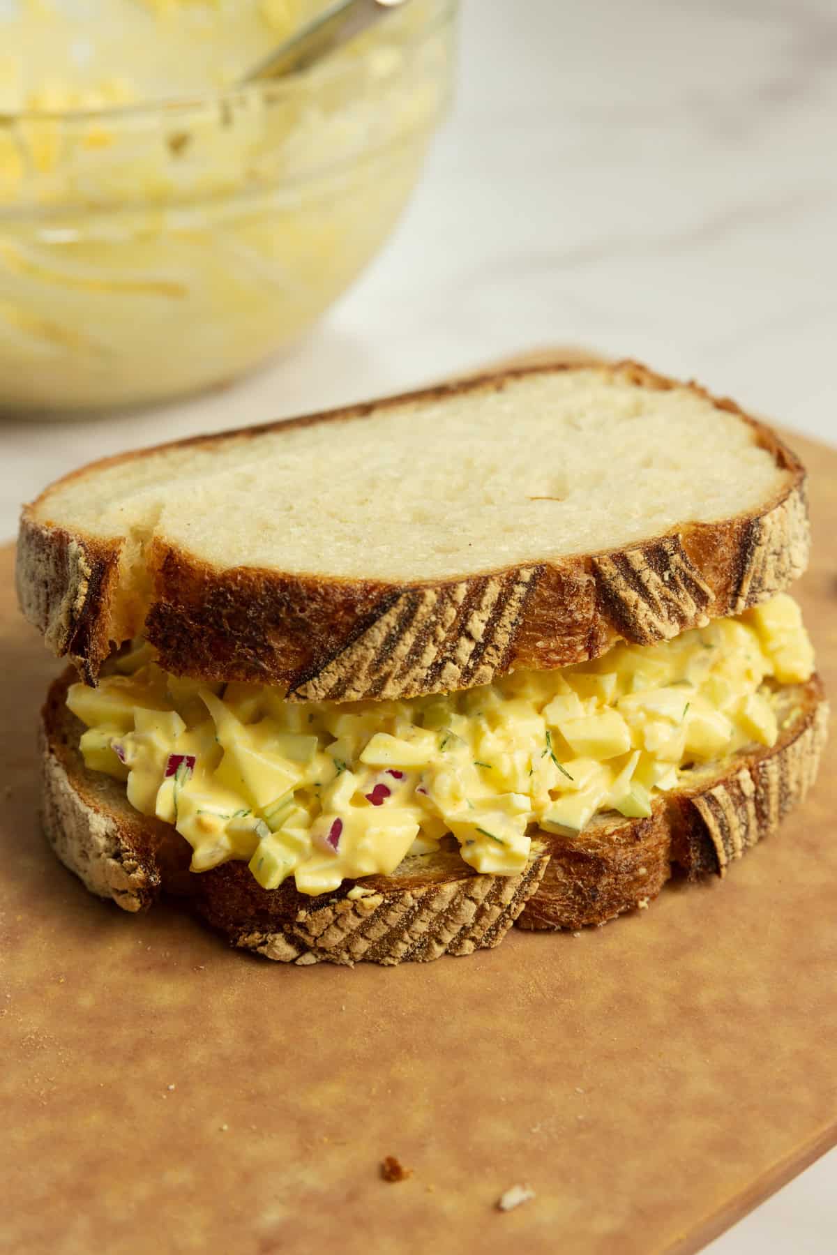 An egg salad sandwich sitting on a cutting board.