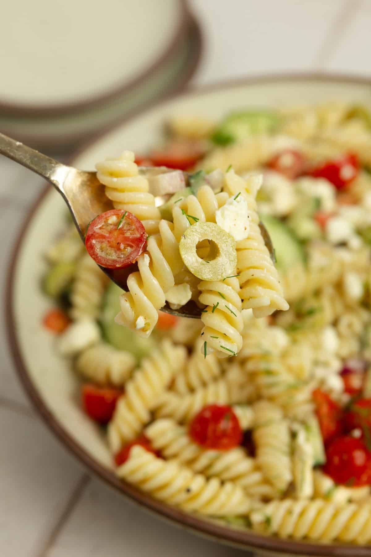 Forkful of Greek pasta salad with a bowl of salad in the background. 