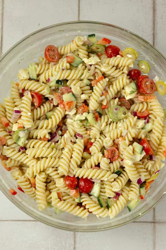 Pasta salad tossed together in a glass bowl.