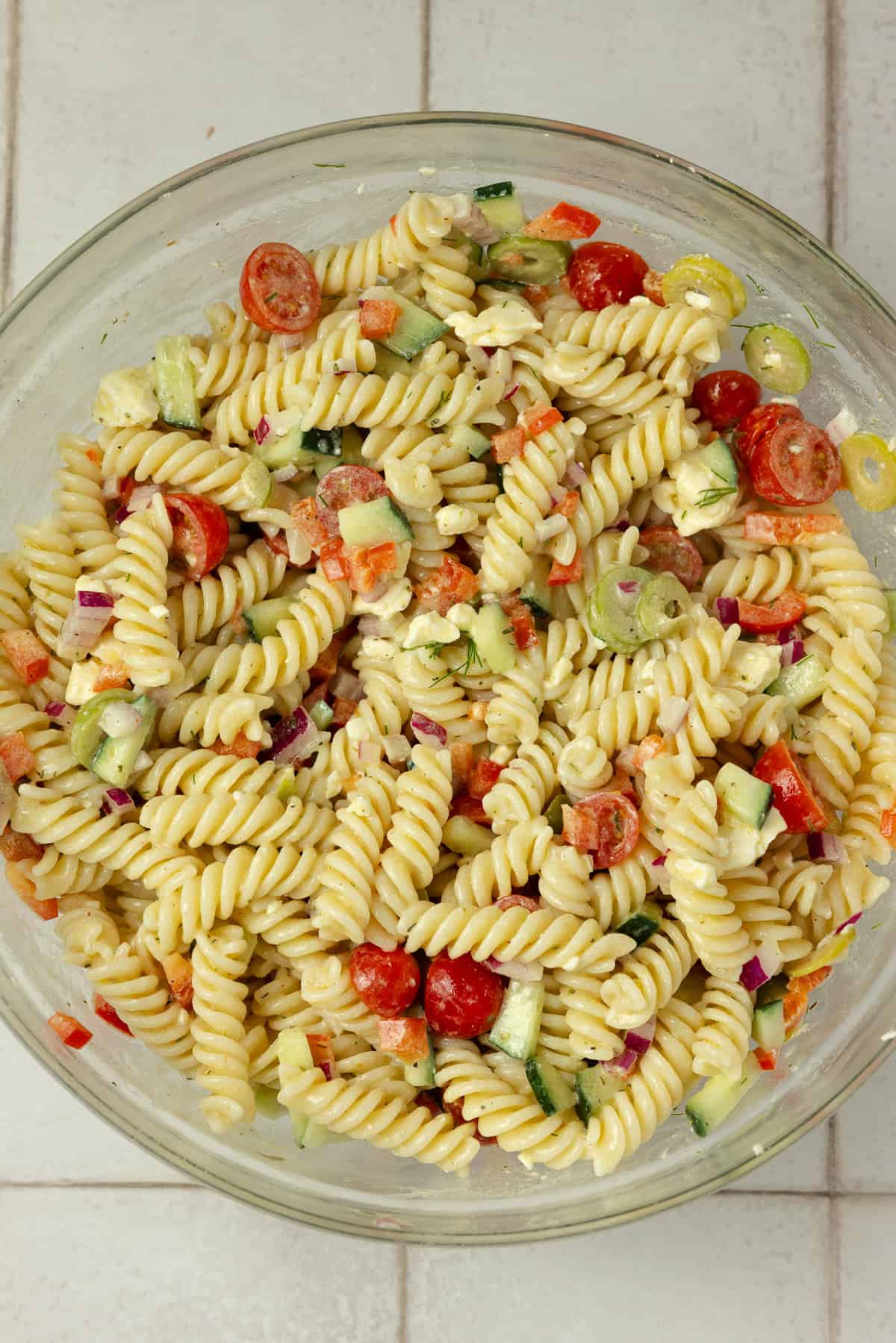 Pasta salad tossed together in a glass bowl.