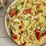 Greek pasta salad filled with pasta, olives, tomatoes, cucumbers, and feta in a large bowl.