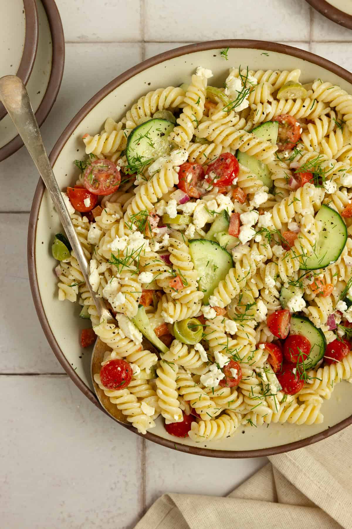 Greek pasta salad filled with pasta, olives, tomatoes, cucumbers, and feta in a large bowl.