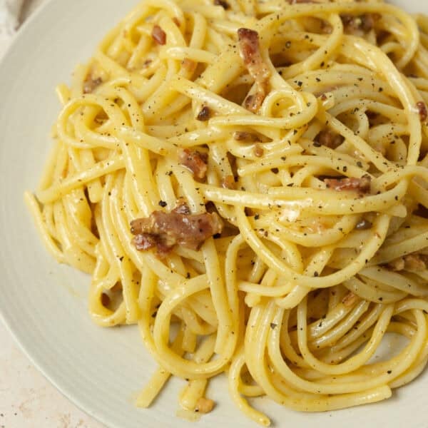 a plate full of pasta carbonara garnished with cracked pepper and grated parmesan.