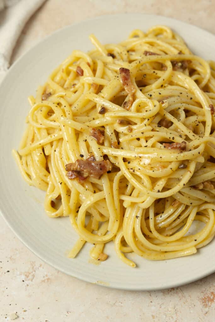 A plate full of pasta carbonara garnished with cracked pepper and grated parmesan.