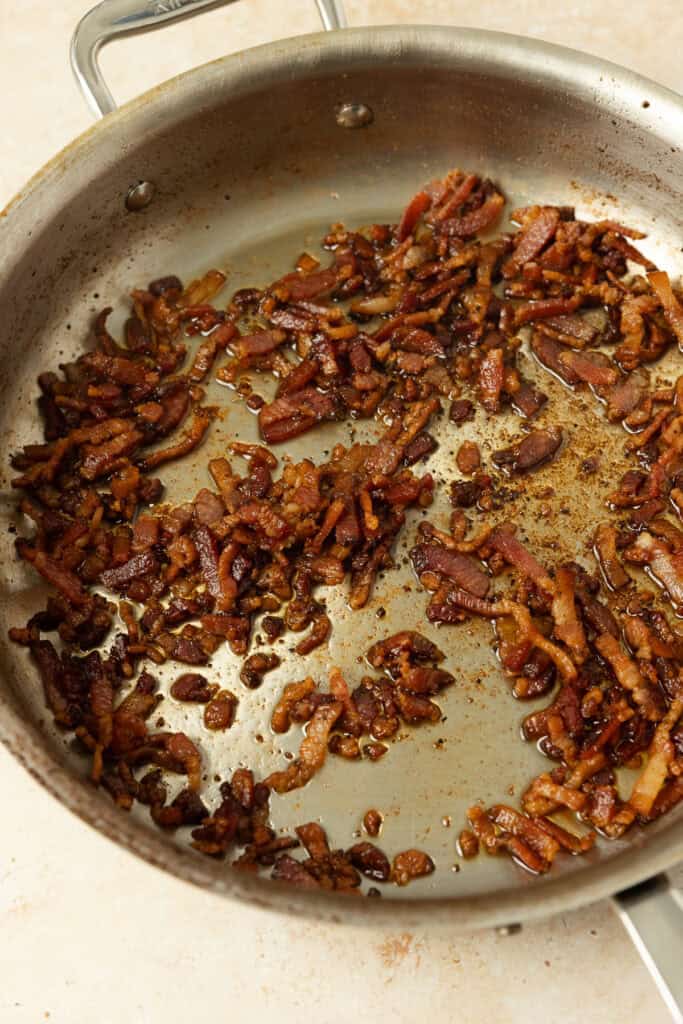 Pieces of bacon cooking in a skillet.