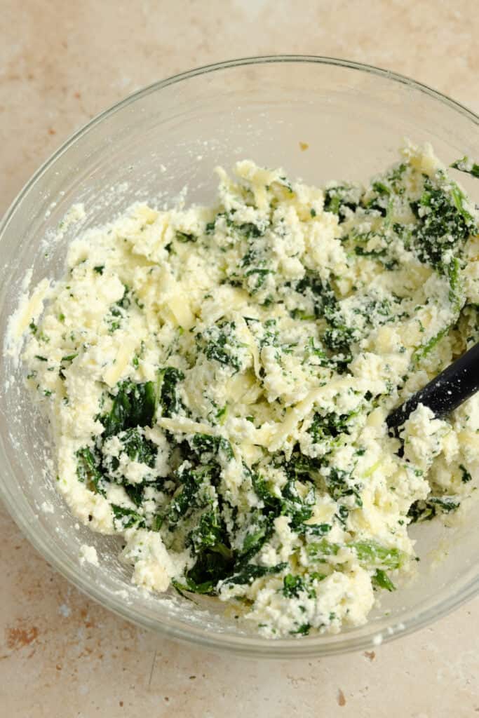 Ricotta, parmesan, and mozzarella mixed with spinach in a bowl.