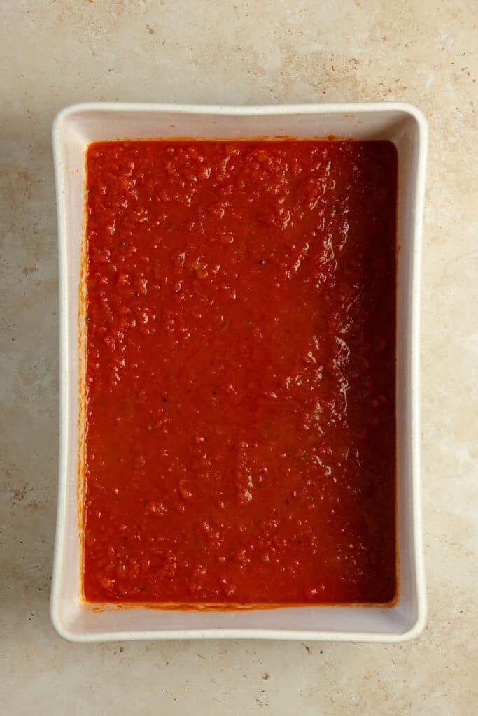 Marinara sauce in the bottom of an 8 inch by 9 inch dish.