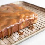 Caramel glaze poured over apple cake on a cooling rack over a baking sheet.