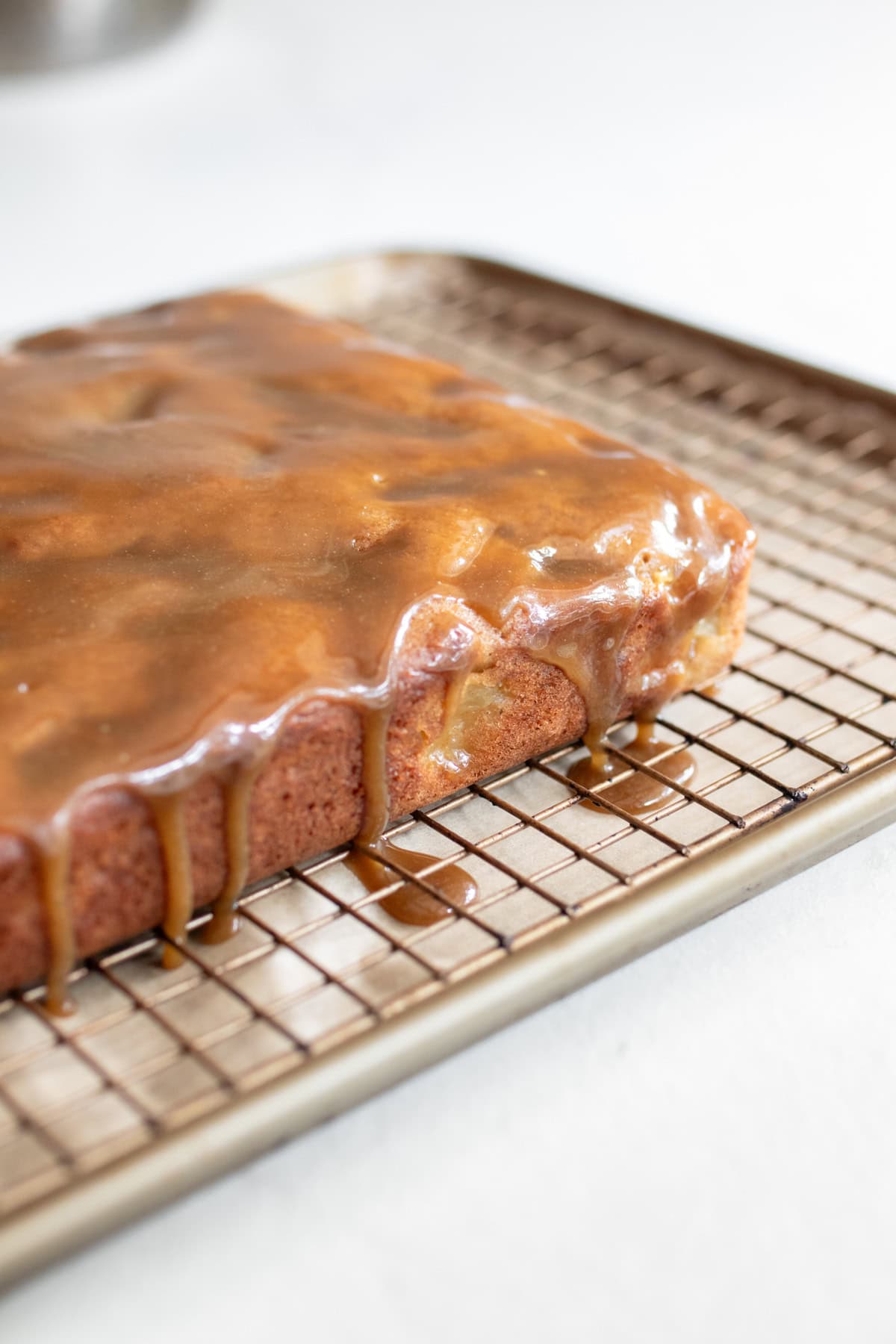 Caramel glaze poured over apple cake on a cooling rack over a baking sheet.