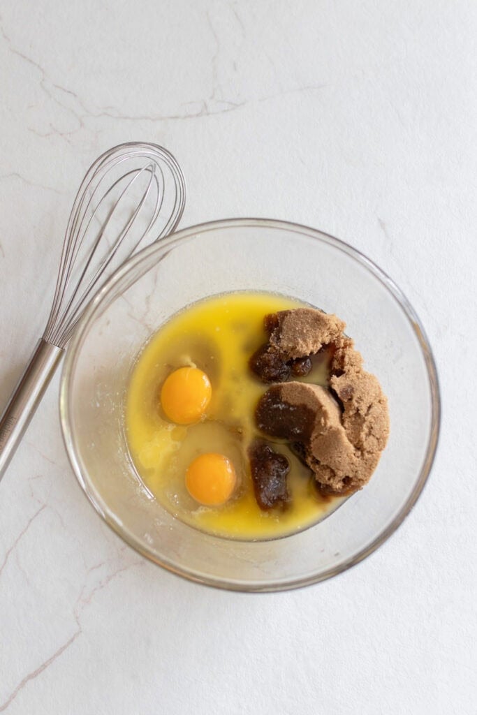 Eggs, brown sugar, melted butter, and other wet ingredients in a glass bowl.