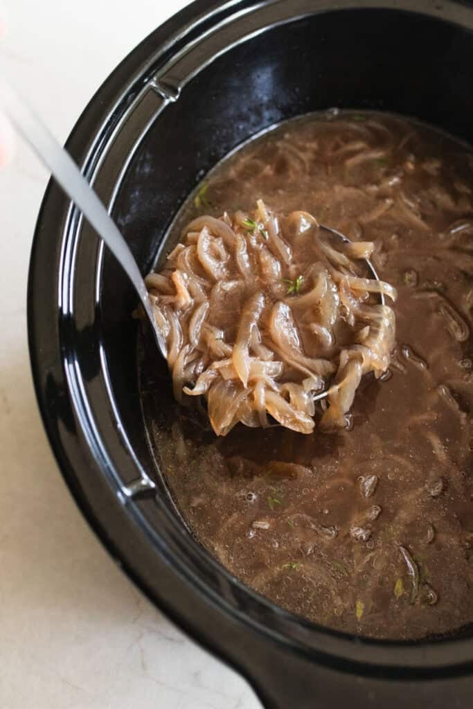 A silver ladle spooning out French onion soup to taste.