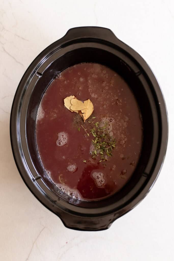 Beef broth, red wine, and spices added to a slow cooker.