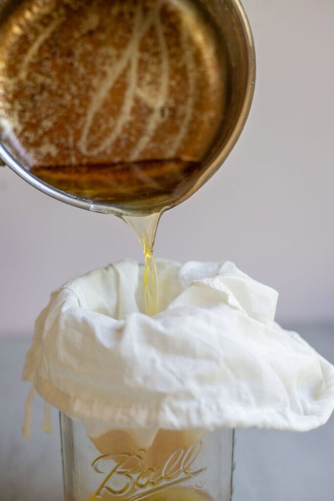 Cooked butter being poured through a cheesecloth. 