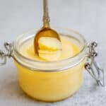 a spoon scooping out ghee from a glass jar.