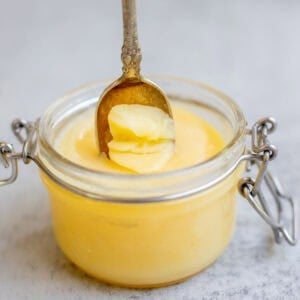 a spoon scooping out ghee from a glass jar.