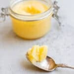a jar full of cooled ghee with a spoon dipped in ghee laying in front of it.