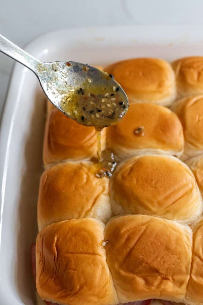 Drizzling seasoned butter over top of Hawaiian rolls.