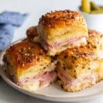 Ham and swiss slider sandwiches stacked on a plate.