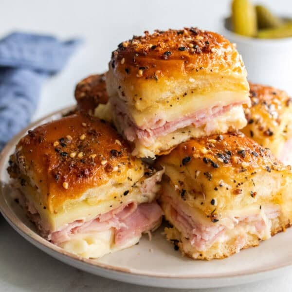 Ham and swiss slider sandwiches stacked on a plate.