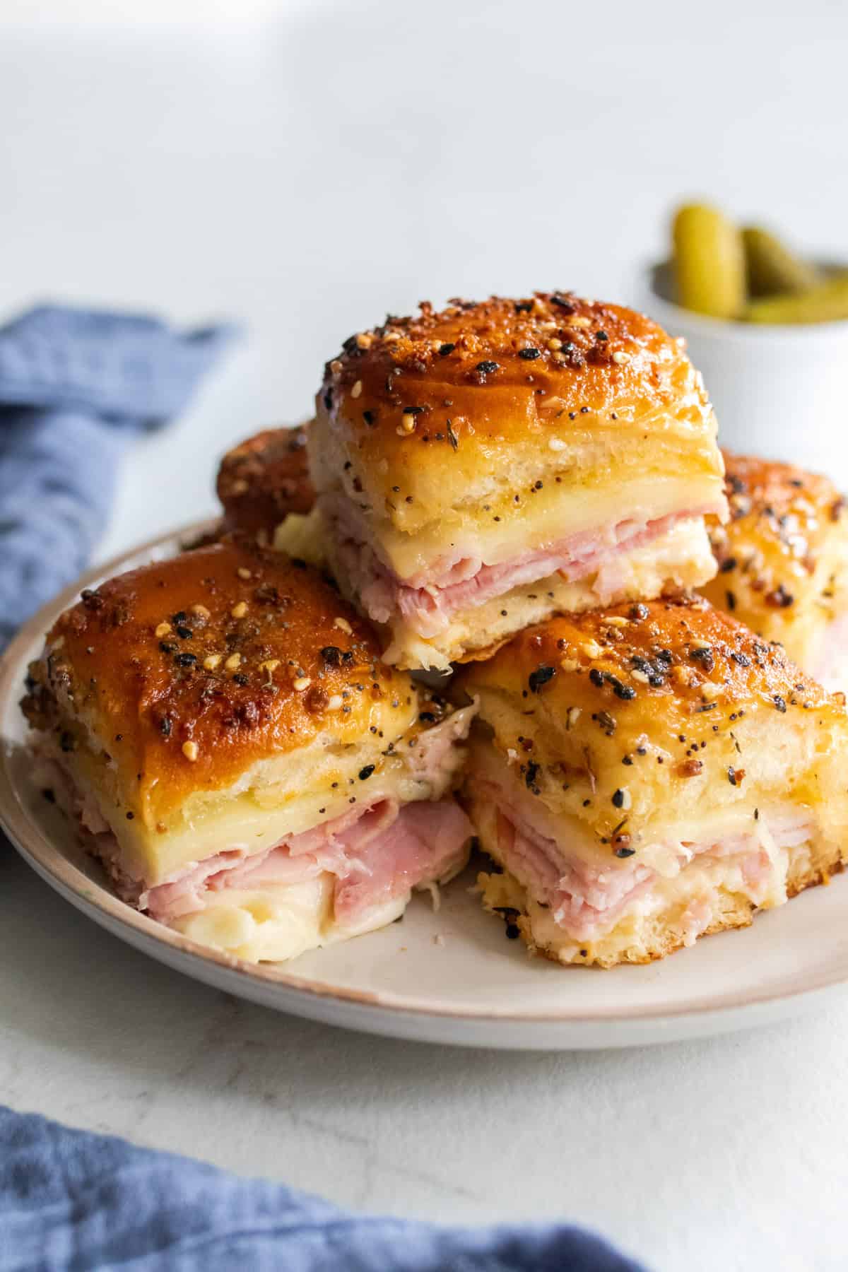 Ham and swiss slider sandwiches stacked on a plate. 