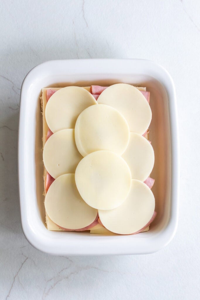 Layers of Swiss, ham and provolone on Hawaiian bread in baking dish. 